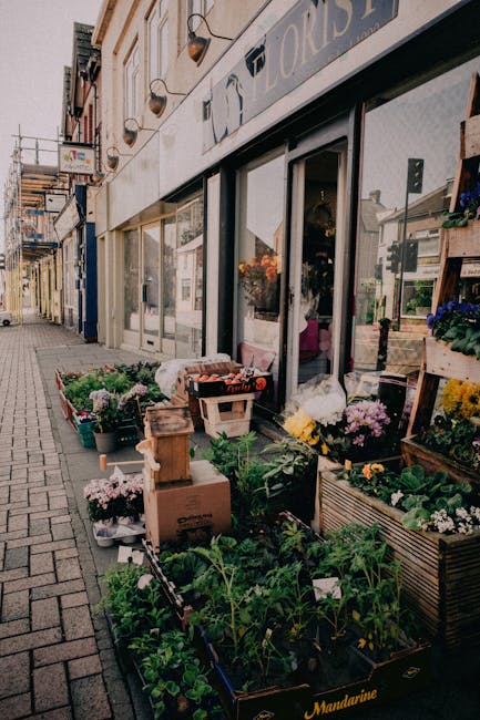 Outdoor display of fresh flowers and potted plants arranged on wooden crates and metal baskets outside Upton Park Florist on Boleyn Road and Green Street. The floral assortment includes colorful chrys
